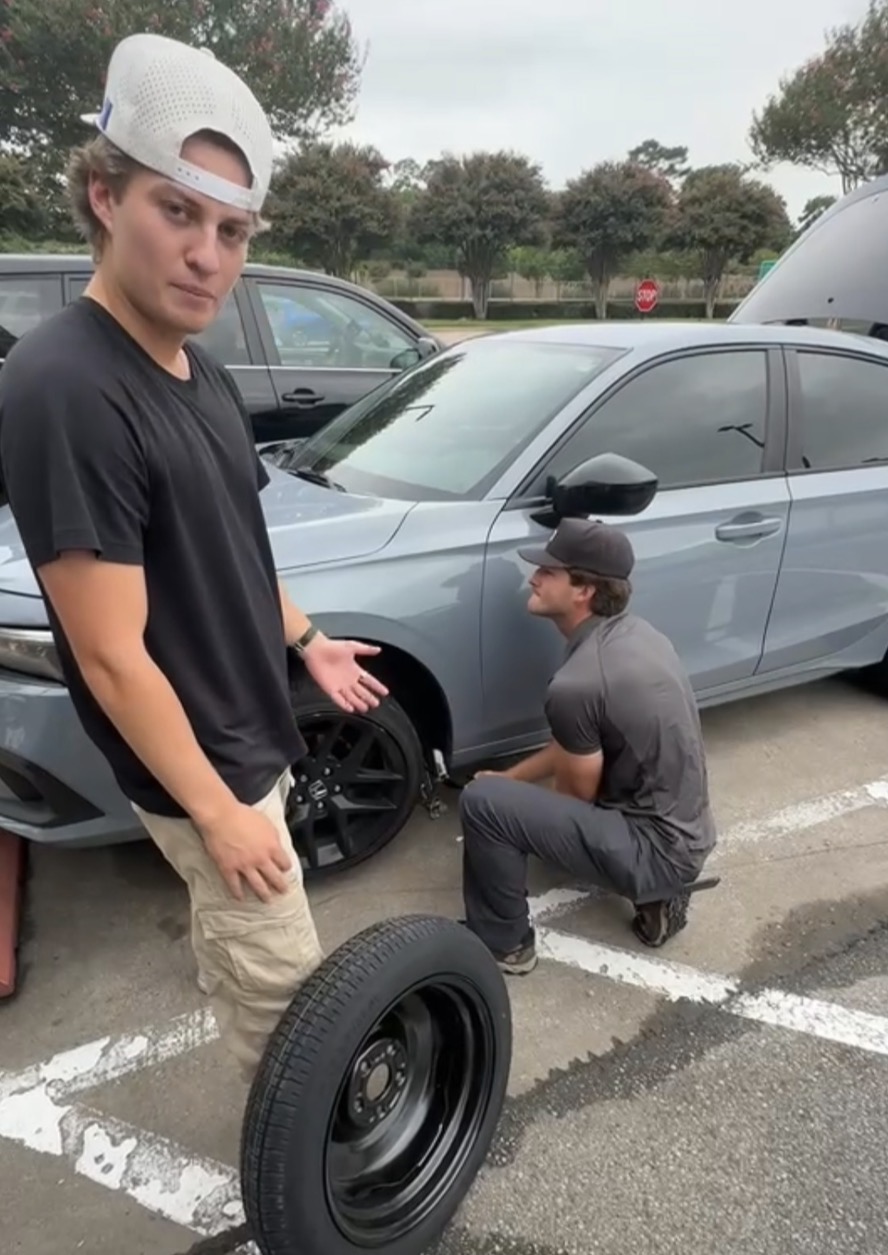 Nate and a teammate changing a flat tire in a parking lot